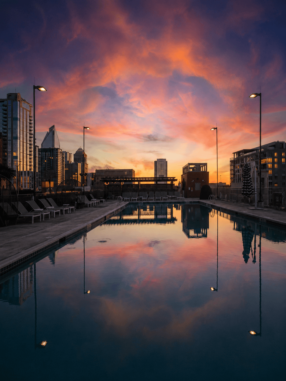 A rooftop pool at sunset reflecting a vivid pink-and-orange sky, the Charlotte skyline glowing on the far side.
